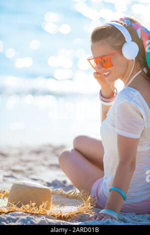 smiling healthy woman in white t-shirt and pink shorts listening to the music with headphones on the seacoast. Stock Photo