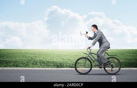 Businessman with megaphone in hand on bike Stock Photo
