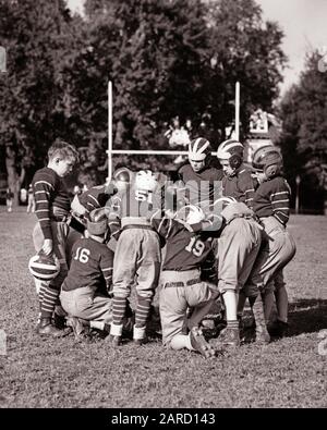 1940s GROUP OF BOYS WEARING FOOTBALL UNIFORMS HUDDLED IN A HUDDLE NEAR GOAL POSTS ON SCHOOL FIELD - f9251 HAR001 HARS GOAL LIFESTYLE NATURE COPY SPACE FRIENDSHIP HALF-LENGTH PHYSICAL FITNESS INSPIRATION MALES ATHLETIC CONFIDENCE B&W GOALS SCHOOLS ACTIVITY GRADE HUDDLE PHYSICAL STRENGTH STRATEGY GRIDIRON RECREATION FALL SEASON NEAR PRIMARY UNIFORMS CONNECTION GOAL POST FLEXIBILITY MUSCLES POSTS COOPERATION FOOTBALLS GRADE SCHOOL GROWTH HUDDLED JUVENILES PRE-TEEN PRE-TEEN BOY TOGETHERNESS AMERICAN FOOTBALL AUTUMNAL BLACK AND WHITE CAUCASIAN ETHNICITY FALL FOLIAGE HAR001 OLD FASHIONED Stock Photo
