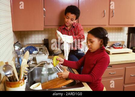 1970s 1980s AFRICAN AMERICAN BOY AND GIRL BROTHER AND SISTER TOGETHER WASHING DISHES BY HAND BOY SITTING ON KITCHEN COUNTER  - kj8830 PHT001 HARS FEMALES BROTHERS HOME LIFE COPY SPACE FRIENDSHIP HALF-LENGTH MALES SIBLINGS SISTERS HIGH ANGLE AFRICAN-AMERICANS AFRICAN-AMERICAN AND BLACK ETHNICITY UP SIBLING CONNECTION SUPPORT COOPERATION JUVENILES PRE-TEEN PRE-TEEN GIRL TOGETHERNESS OLD FASHIONED AFRICAN AMERICANS Stock Photo