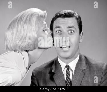 1960s BLONDE WOMAN KISSING SURPRISED BUG-EYED WIDE-EYED MAN ON CHEEK  - r19161 HAR001 HARS COMIC NECK STRONG JOY LIFESTYLE SATISFACTION CELEBRATION FEMALES MARRIED STUDIO SHOT SPOUSE HUSBANDS HOME LIFE COPY SPACE FRIENDSHIP LADIES PERSONS INSPIRATION CARING MALES EXPRESSIONS B&W PARTNER EYE CONTACT BIZARRE BRUNETTE TEMPTATION SUIT AND TIE HUMOROUS HAPPINESS WEIRD HEAD AND SHOULDERS DISCOVERY STRATEGY ZANY COMICAL UNCONVENTIONAL RELATIONSHIPS CONNECTION CONCEPTUAL COMEDY FRIENDLY WACKY IDIOSYNCRATIC PERSONAL ATTACHMENT AFFECTION AMUSING ECCENTRIC EMOTION MID-ADULT MID-ADULT MAN MID-ADULT WOMAN Stock Photo