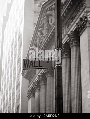 1960s 1970s WALL STREET SIGN ON LAMPPOST IN FRONT OF NEW YORK STOCK EXCHANGE BUILDING  - s17179 HAR001 HARS OPPORTUNITY OCCUPATIONS STOCKS REAL ESTATE TRADING CONCEPTUAL NEW YORK NEW YORK STOCK EXCHANGE STRUCTURES NYSE EDIFICE IN FRONT OF LAMPPOST BLACK AND WHITE HAR001 OLD FASHIONED Stock Photo