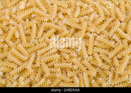 Raw dried extruded fusilli pasta texture. Staple food of Italian cuisine. Culinary background from short uncooked helical pastas for cooking side dish. Stock Photo