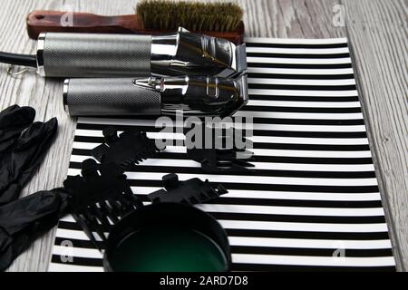 Haircut machines, nozzles of different sizes, combs and gels for styling, laid out on a beautiful black white striped background which stands on a gra Stock Photo