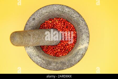 Top view close up on isolated gray basalt stone mortar with pestle and red pepper corns, yellow blank background Stock Photo