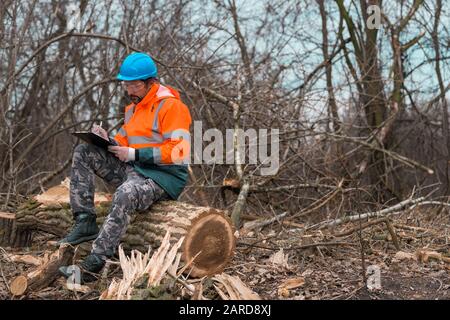 Forestry technician writing notes on clipboard notepad paper in forest during logging deforestation process Stock Photo