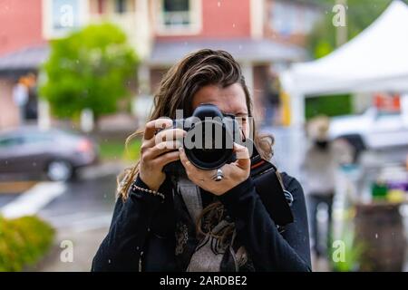 Portrait of professional female photographer wearing warm clothing and taking photograph from her camera on city street in summer season Stock Photo