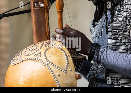 Midsection of male artist with dreadlocks wearing bracelets while performing traditional wooden harp kora during event with focus on foreground Stock Photo