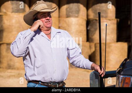 Farmer on cell phone near truck with antennas hay bales in shed in background Stock Photo