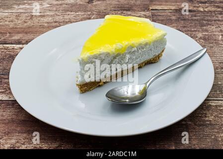 Slice of lemon cheesecake on white plate, wooden table Stock Photo