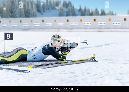 Biathlete lies and shoots a target at a 20 km race. Athlete with modern sports equipment for competition Stock Photo