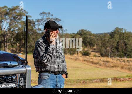 Man on mobile phone, looking away , next to truck with antennas. Paddock in background Stock Photo