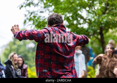 Rear view of carefree man wearing red and blue checked shirt while dancing and enjoying against people in city during summer rainy season Stock Photo