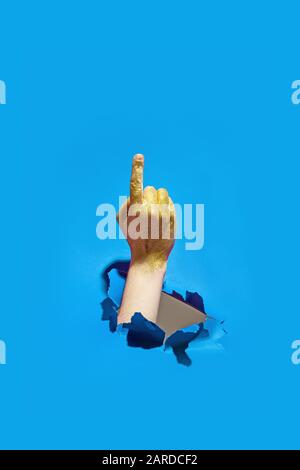 Gesture male hand in golden glitter through torn blue paper. Stock Photo