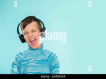 Kid enjoying music on his headphones, listening to music. Handsome young stylish kid in headphones standing against blue background and smiling Stock Photo