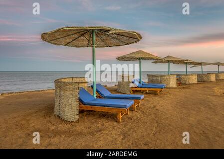 a tropical beach with sunbeds and shelters in a row at the sunset, el Gouna, Egypt, January 12, 2020 Stock Photo