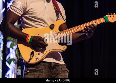 Closeup of african professional male musician wearing white t-shirt and playing electric guitar on stage at auditorium during night Stock Photo