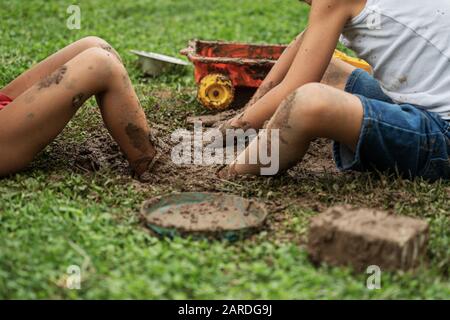 Two boys playing with mud in backyard digging their foot in the dirt. Stock Photo