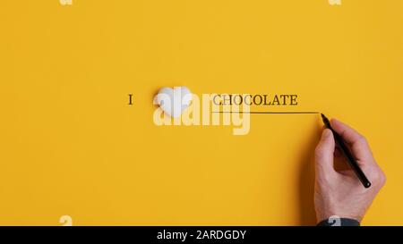 Male hand writing an I love chocolate sign with black marker over yellow background. Stock Photo