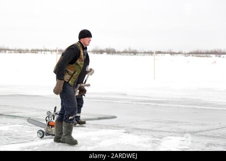 A worker walks on the ice of a frozen lake, with a sawing machine Stock Photo