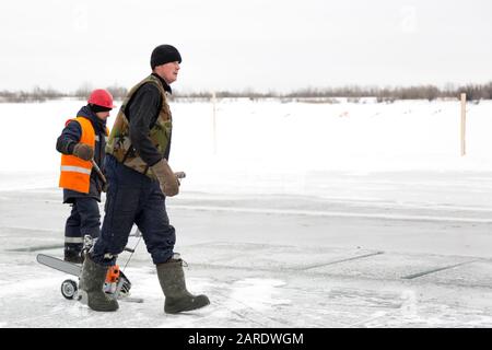 A worker walks on the ice of a frozen lake, with a sawing machine Stock Photo