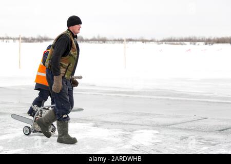 A worker walks on the ice of a frozen lake, with a sawing machine Stock Photo