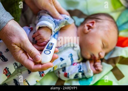 A close up selective focus view on the hands of a family doctor using a medical thermometer under the arm of a newborn baby boy, with copy space Stock Photo