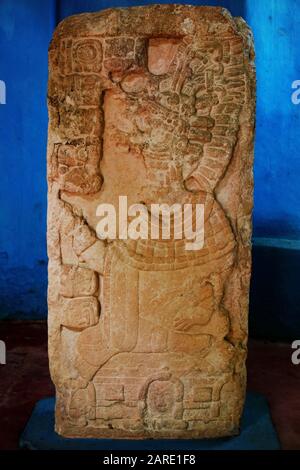 Stele 20 depicts an unusually seated leader wearing an elaborate mask and headdress, while glyphs run down the left side of the stone in the ancient M Stock Photo