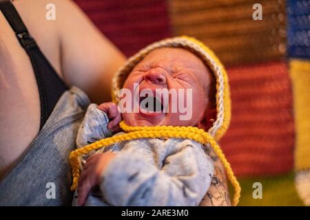 A close up view of a newborn infant in the arms of mother in hours after childbirth, wrapped in blankets to stay warm, crying baby with caring parent Stock Photo