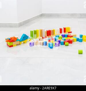 Different color and shape wooden toy building blocks in home on grey tiles floor. Stock Photo
