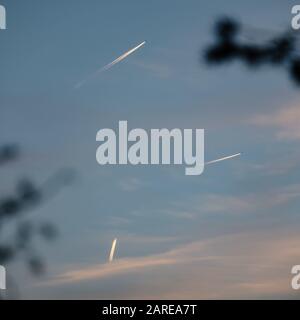 Low angle view of planes leaving tracks on the sky during the sunset Stock Photo