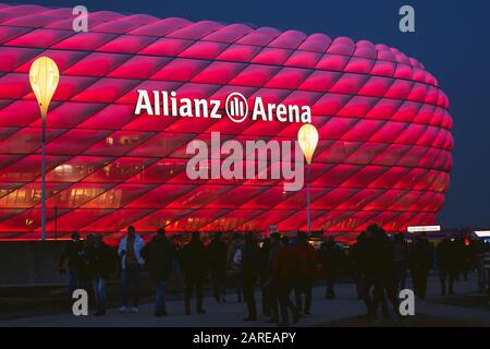 MUNICH, GERMANY - Jan 25, 2020: Illuminated arena of german football club FC Bayern München. Red light of Allianz Arena with fans walking to see the m