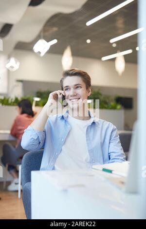 Portrait of smiling young man lspeaking by smartphone while working with laptop in office Stock Photo