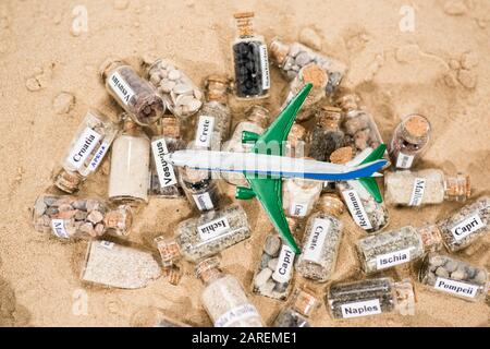 Glass test-tube with sand of different summer vacation countries. Located in sand with small airplane. Stock Photo