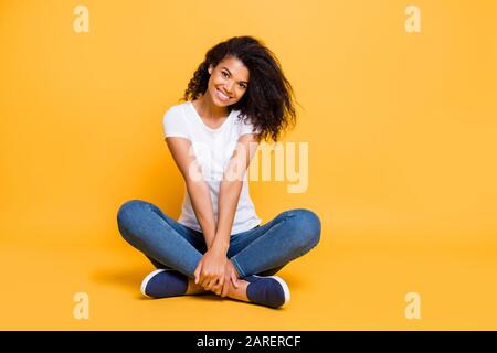 Full length body size photo of cheerful positive cute nice charming pretty girl in jeans denim footwear sitting with legs crossed isolated over vivid Stock Photo