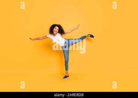 Full length body size photo of cheerful wavy curly trendy girl wearing jeans denim ecstatic pretending to be flying like airplane isolated over vivid Stock Photo