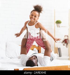 Black dad lifting kid up, playing together in bed Stock Photo