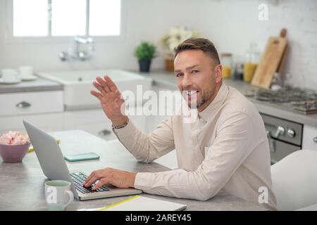 Good-looking bearded man sitting in the kitchen and waving his hand Stock Photo