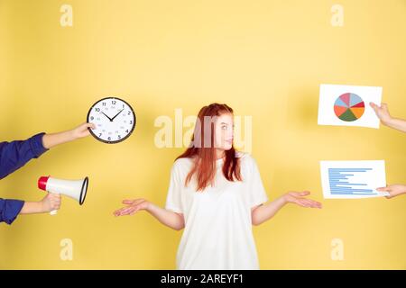 Choosing. Caucasian young woman's portrait on yellow studio background, too much tasks. How to manage time right. Concept of office working, business, finance, freelance, self management, planning. Stock Photo
