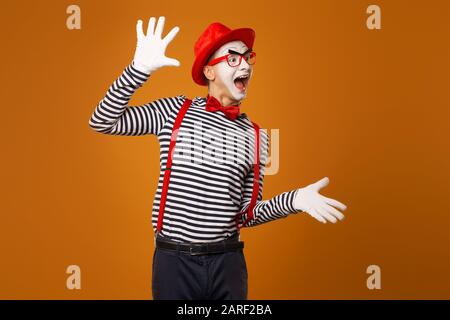 Smiling mime man in red hat, white gloves and striped t-shirt on blank orange background in studio Stock Photo