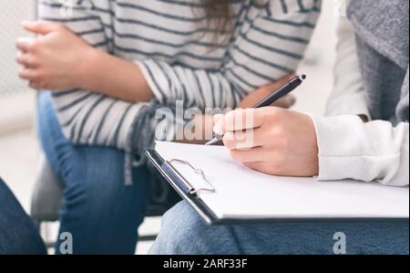 Specialist taking notes during psychotherapy session with young woman Stock Photo