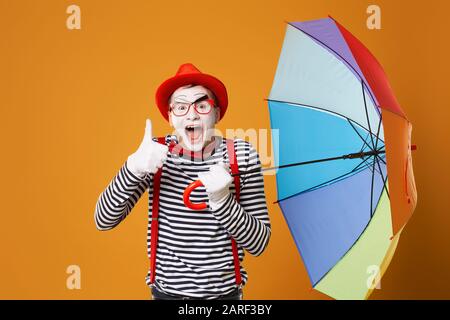 Cheerful mime with multi-colored umbrella isolated on blank orange background in studio Stock Photo