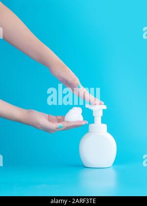 plastic pump bottle and mousse foam or cleansing foam on woman hand isolated on blue background, vertical with copy space. cleaning concept Stock Photo