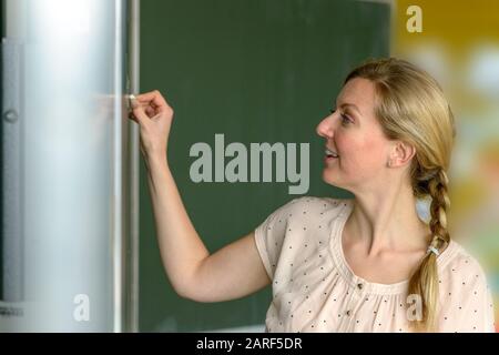Motivated happy school teacher writing on the chalkboard with a smile while teaching her class Stock Photo