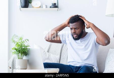 Shocked african guy looking at broken laptop Stock Photo