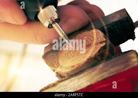 Woman using a high speed rotary multi tool to engrave ornament on slice of wood. Tool could be used as grinder Stock Photo