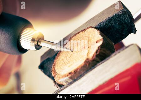 Woman using a high speed rotary multi tool to engrave ornament on slice of wood. Tool could be used as grinder Stock Photo