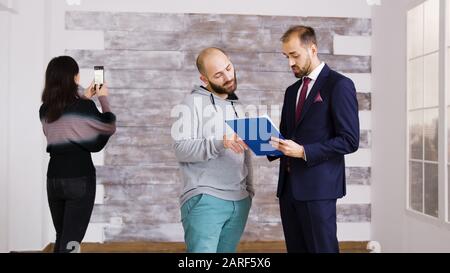 Real estate agent talking with client in empty apartment. Woman taking pictures in empty apartment. Stock Photo