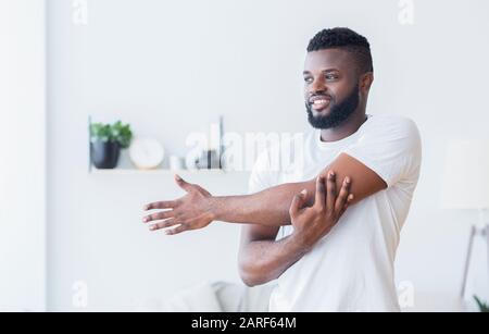 Young black man training and stretching arm at home Stock Photo