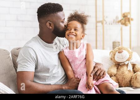 Loving black dad kissing his happy little daughter